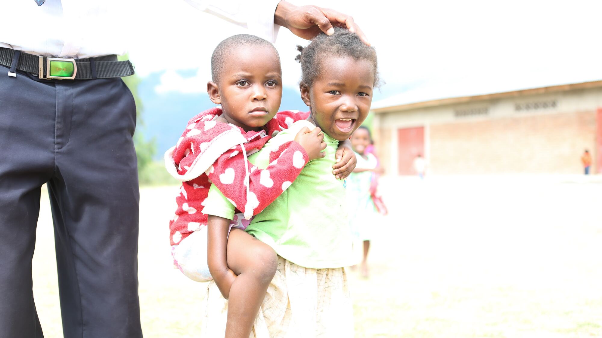 A caregiver lifts two smiling children into the air outside the BCV preschool in Malawi