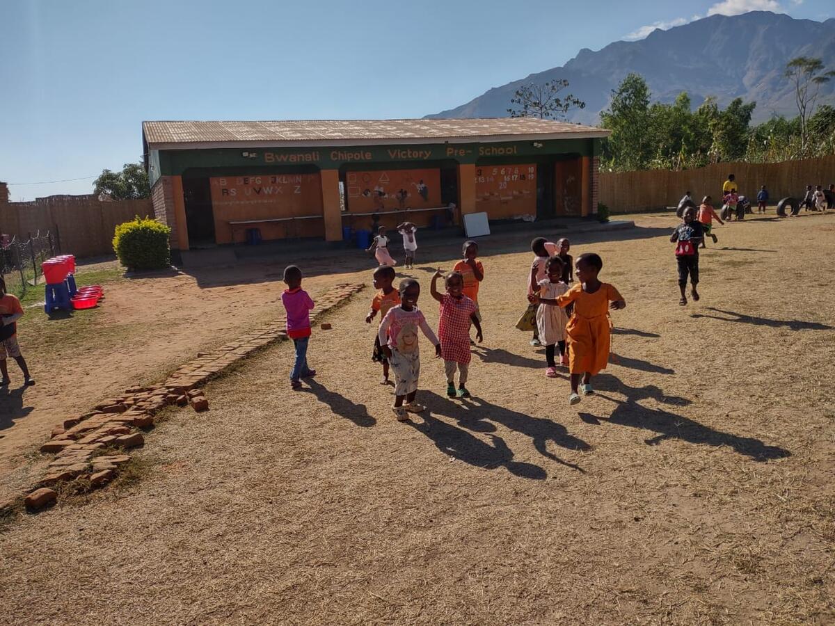 Children running and laughing outside the Bwanali Chipole Victory Pre-School building
